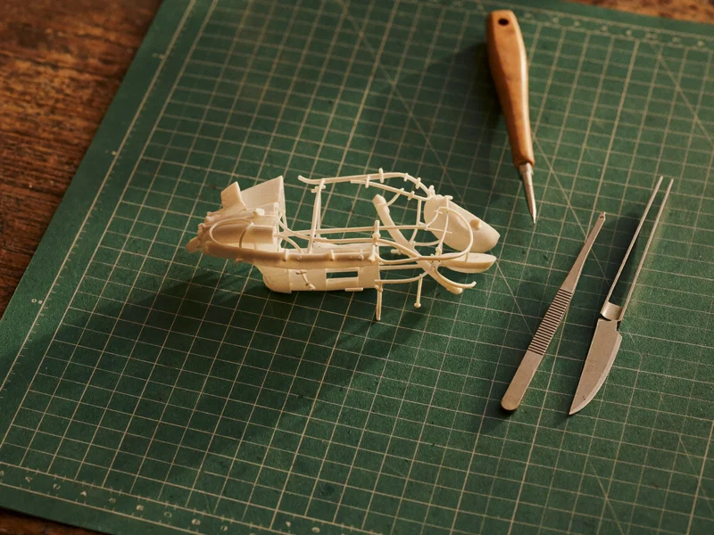 Unbemalter Modellbausatz mit Schneidematte, Pinzette und Cuttermesser von oben